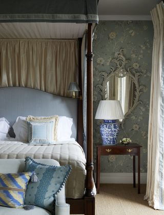 bedroom with four poster bed, duck egg blue color scheme, floral wallpaper, small couch at foot of bed, blue and white chinoiserie style lamp base, ornate mirror