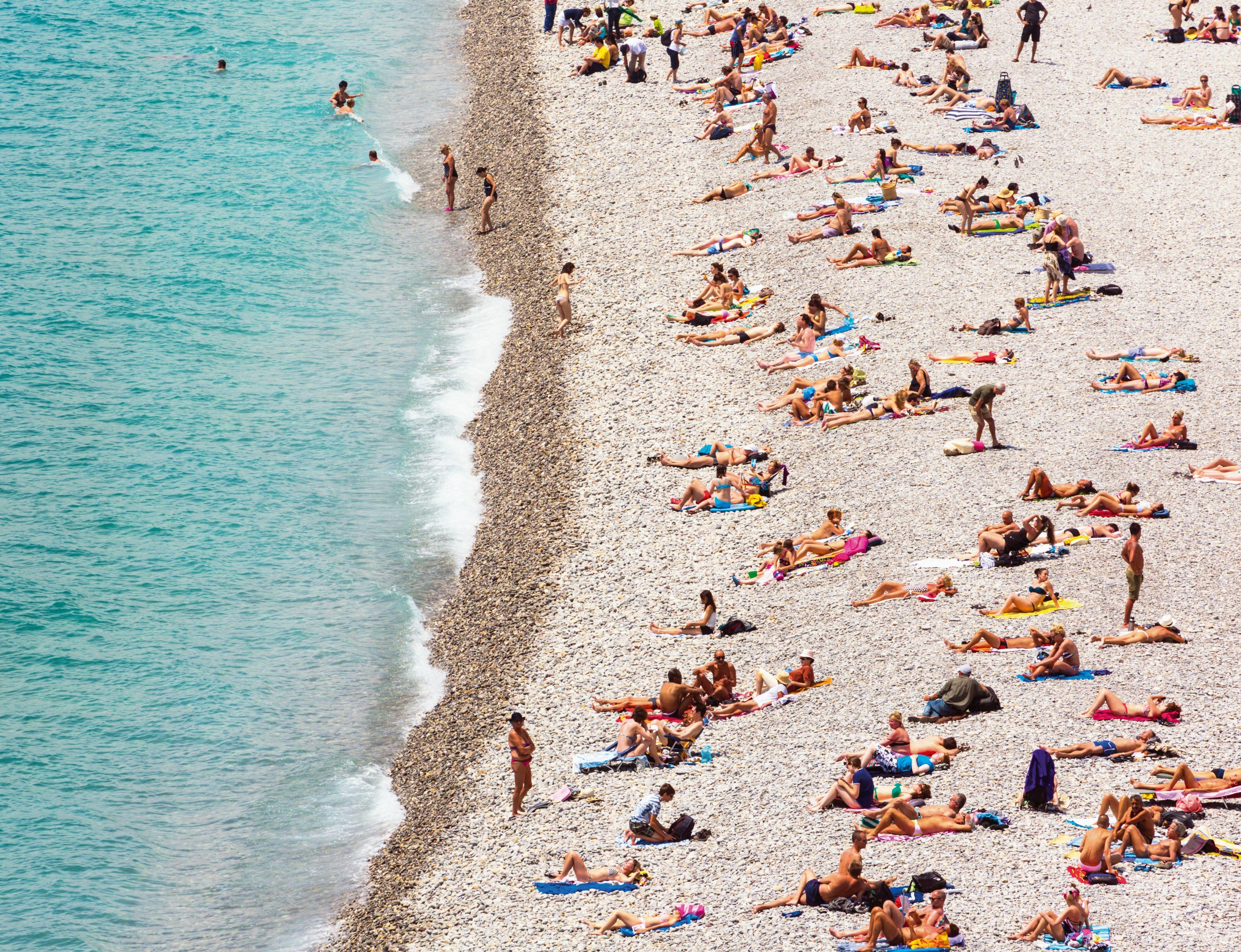 Bathers on a pebble beach infront of a turquoise sea