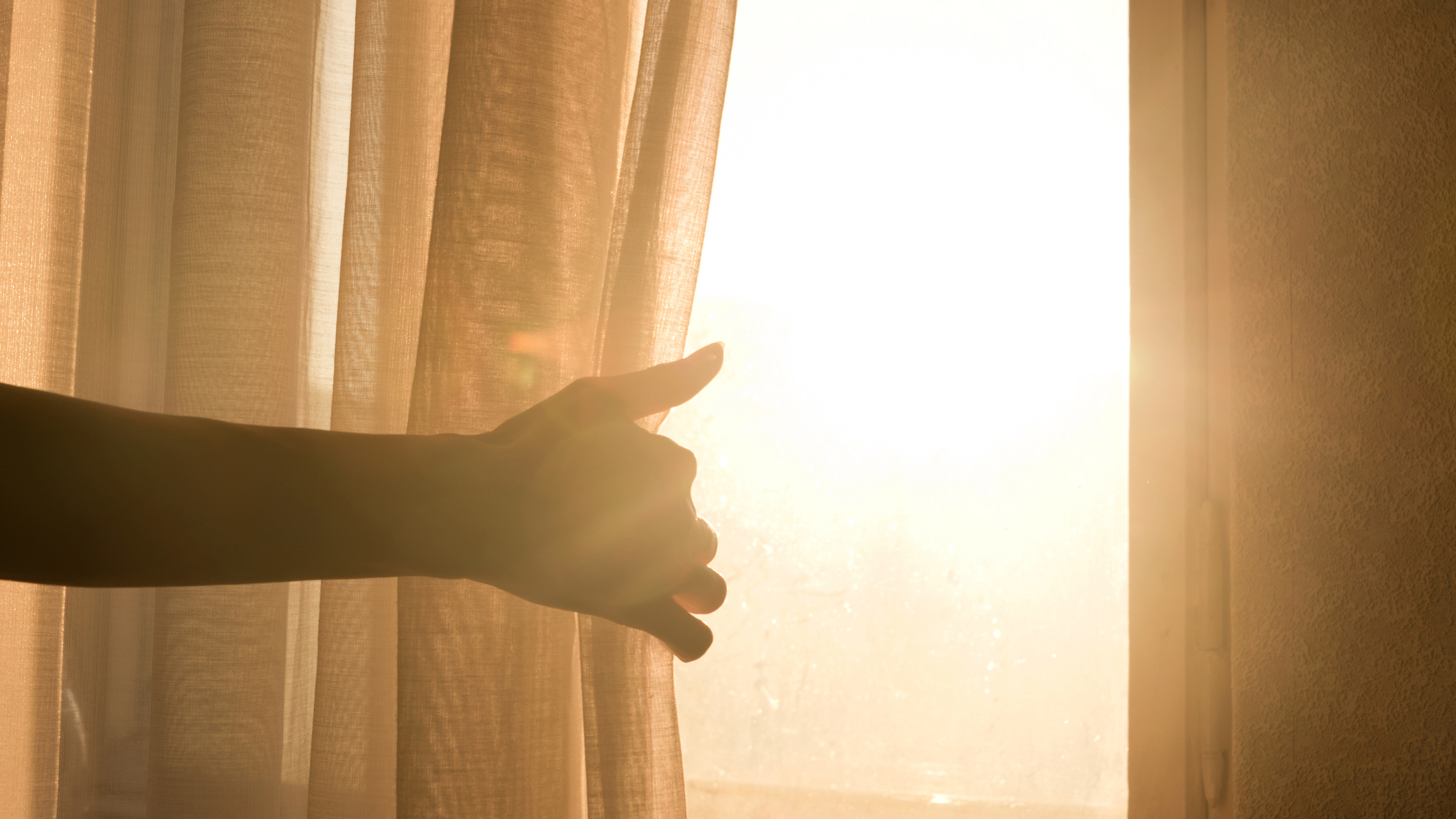 Ein Mann öffnet an einem schönen sonnigen Morgen die Vorhänge