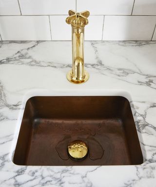 A custom kitchen sink with brass faucet and marble worktop