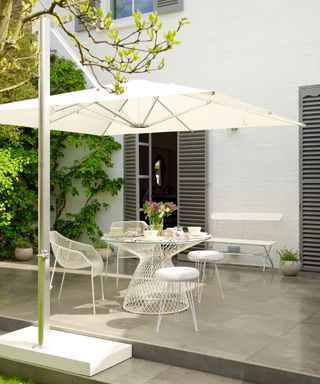 A garden patio with a white bistro set and moveable parasol
