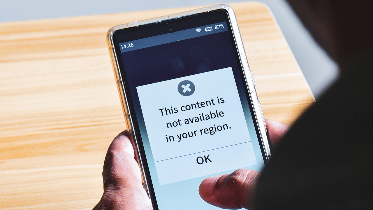 Person holding a phone displaying "This content is not available in your region" warning