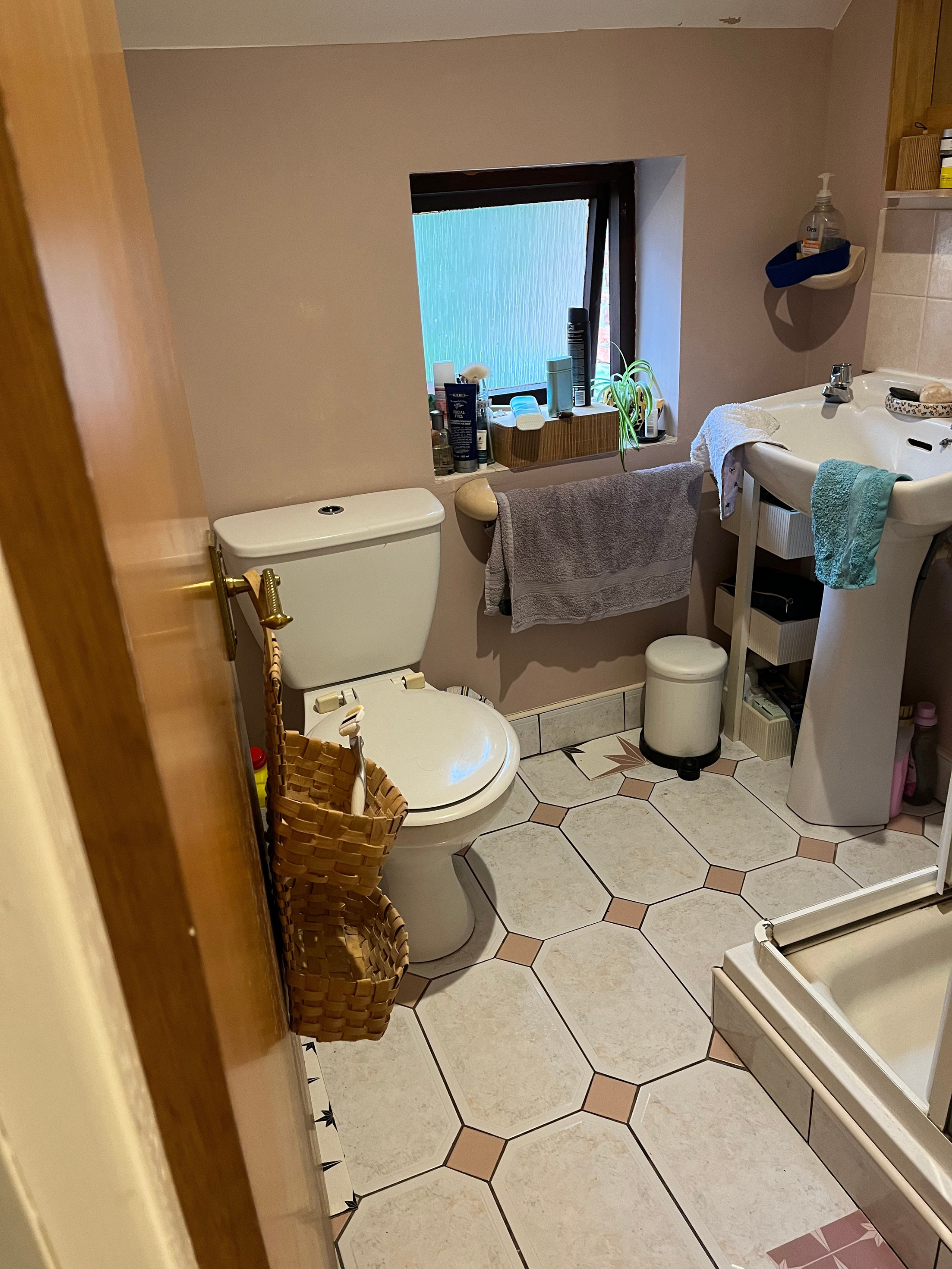A bathroom floor prior to renovation with dated floor tiles and sample peel and stick vinyl tiles on the floor