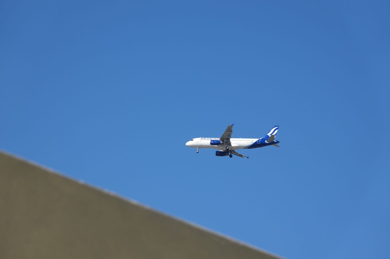 Aegean Airlines passenger plane flying through a clear blue sky with its landing gear lowered.