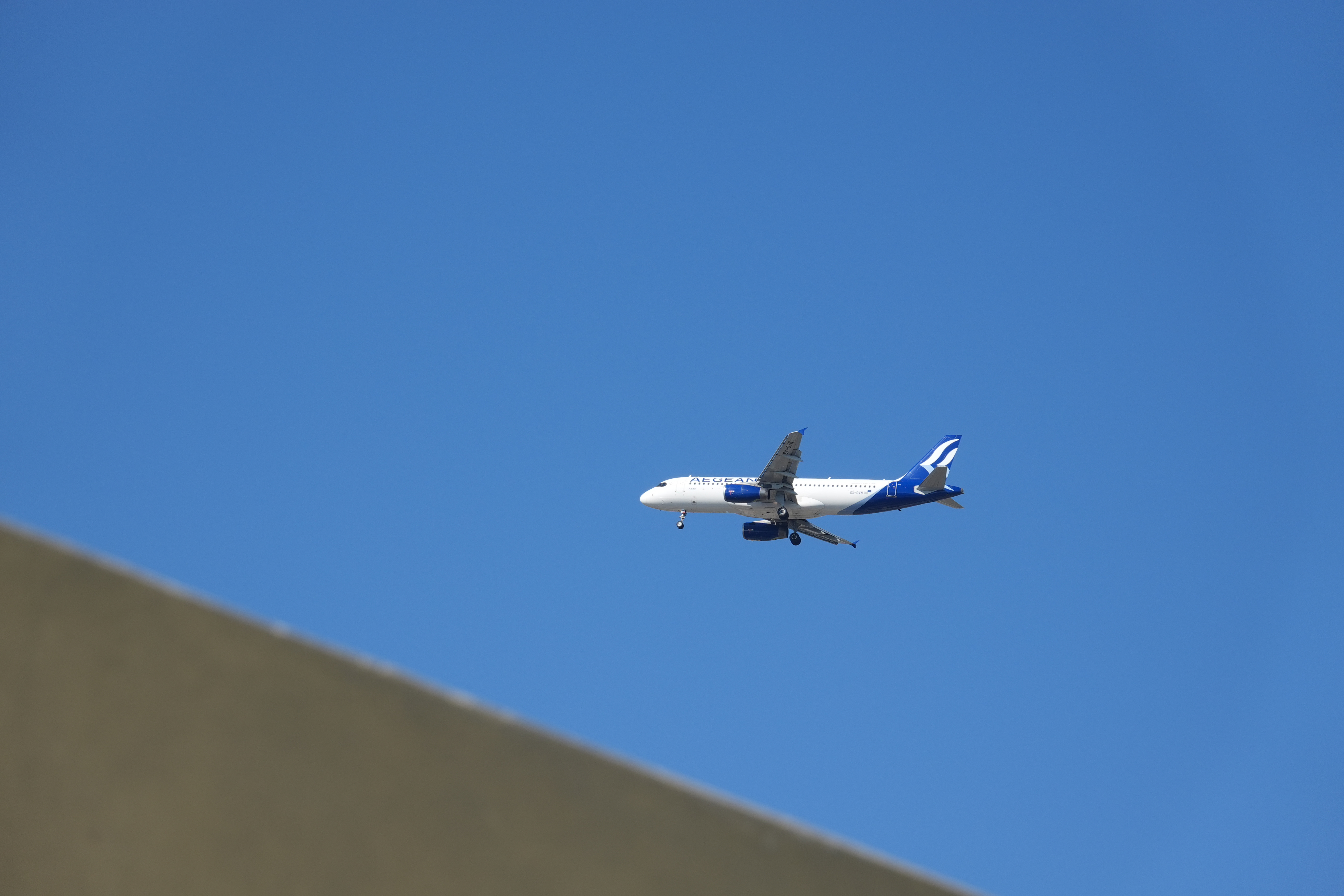Aegean Airlines passenger plane flying through a clear blue sky with its landing gear lowered.