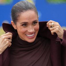 Meghan Markle pulling up the collar on her coat and smiling