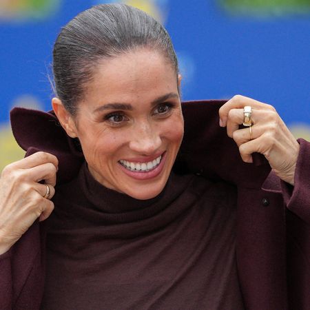 Meghan Markle pulling up the collar on her coat and smiling