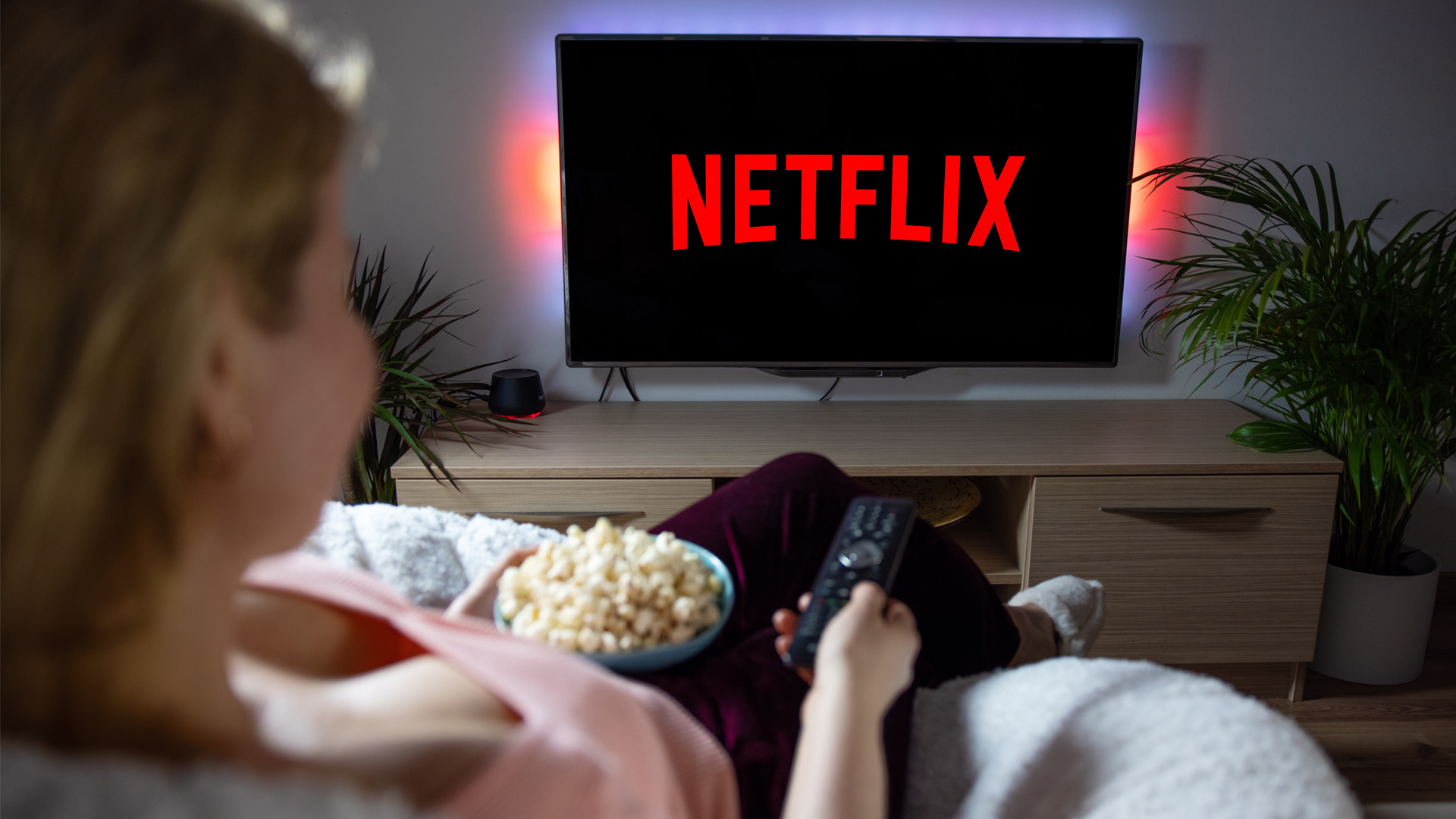 A woman watches Netflix on her TV with a bowl of popcorn in her hand