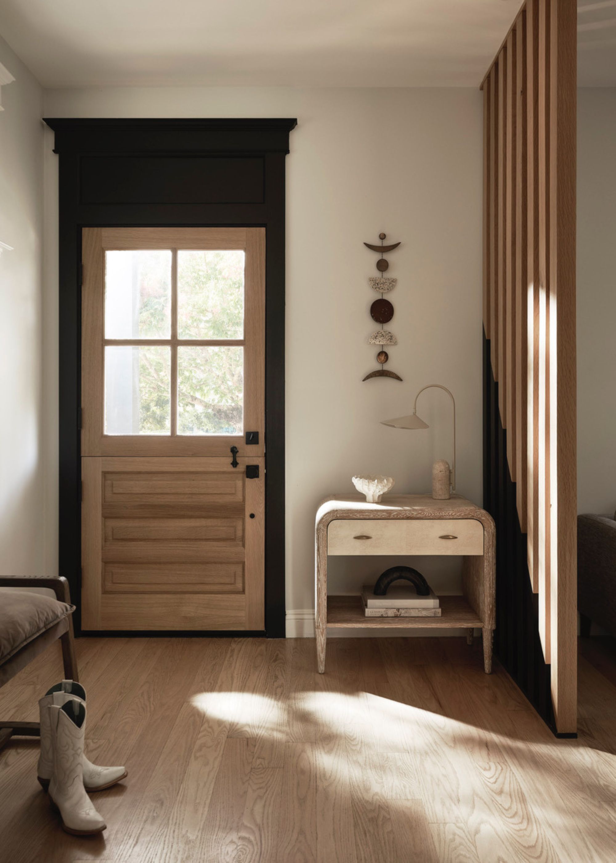 modern entryway with warm white walls, light wooden door and floors, wooden wall divider