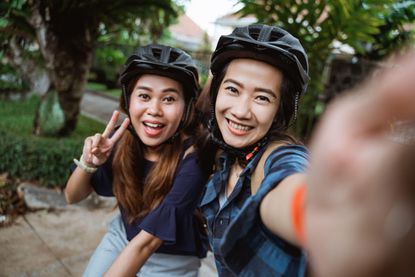 Two young woman wearing helmet and bags with camera smartphone make a photo when ride a bike before go to campus