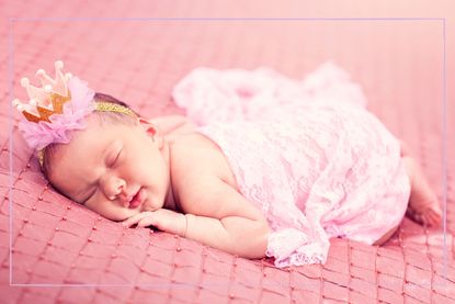 A newborn baby sleeping while wearing a pink crown