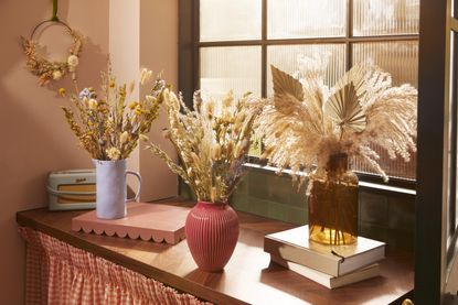 image of dried flowers in three vases on console table by a window 