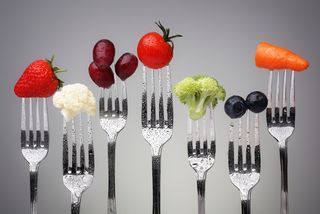 A row of forks, each holding a bit of a different food.