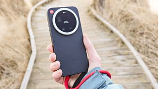 The Leica Leitzphone in person's hand with a wooden boardwalk backdrop