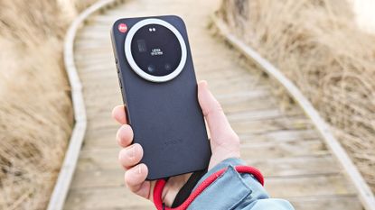 The Leica Leitzphone in person's hand with a wooden boardwalk backdrop