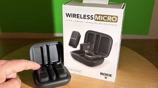 Rode Wireless Micro next to its retail box with a finger pointing to the microphone