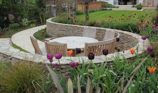 sloping garden ideas: curved garden path and garden walls leading down to a dining area surrounded by tulips
