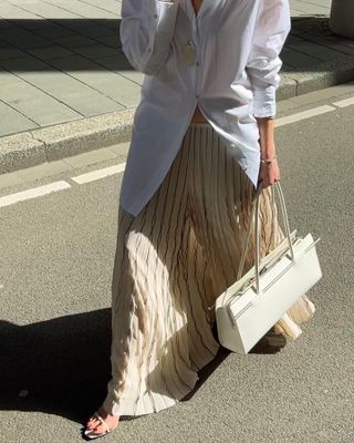 Wanita mengenakan rok dengan sandal dan tas putih