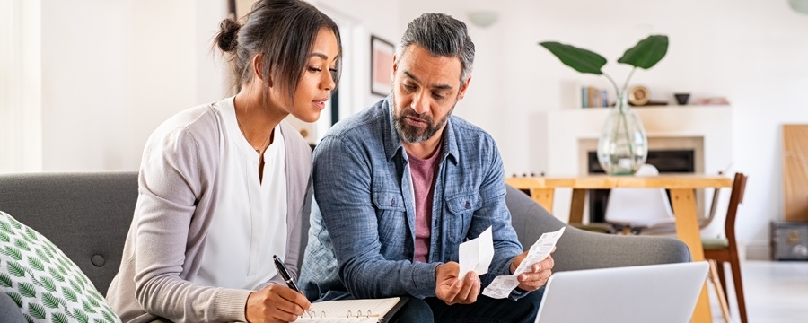 Bi-racial straight couple reviewing finances with laptop and receipts