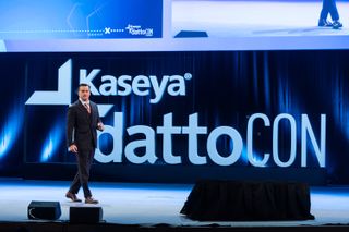 Kaseya CEO Fred Voccola walking across a stage with the words Kaseya Datto con displayed behind him