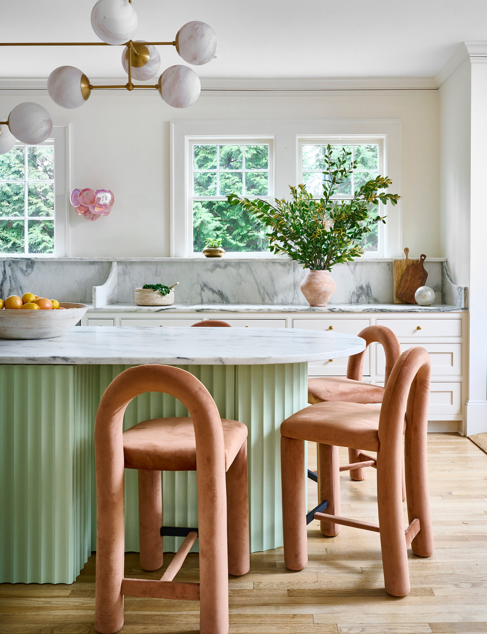 Cheerful eat-in kitchen area featuring a mint green island surrounded by contemporary peach dining chairs