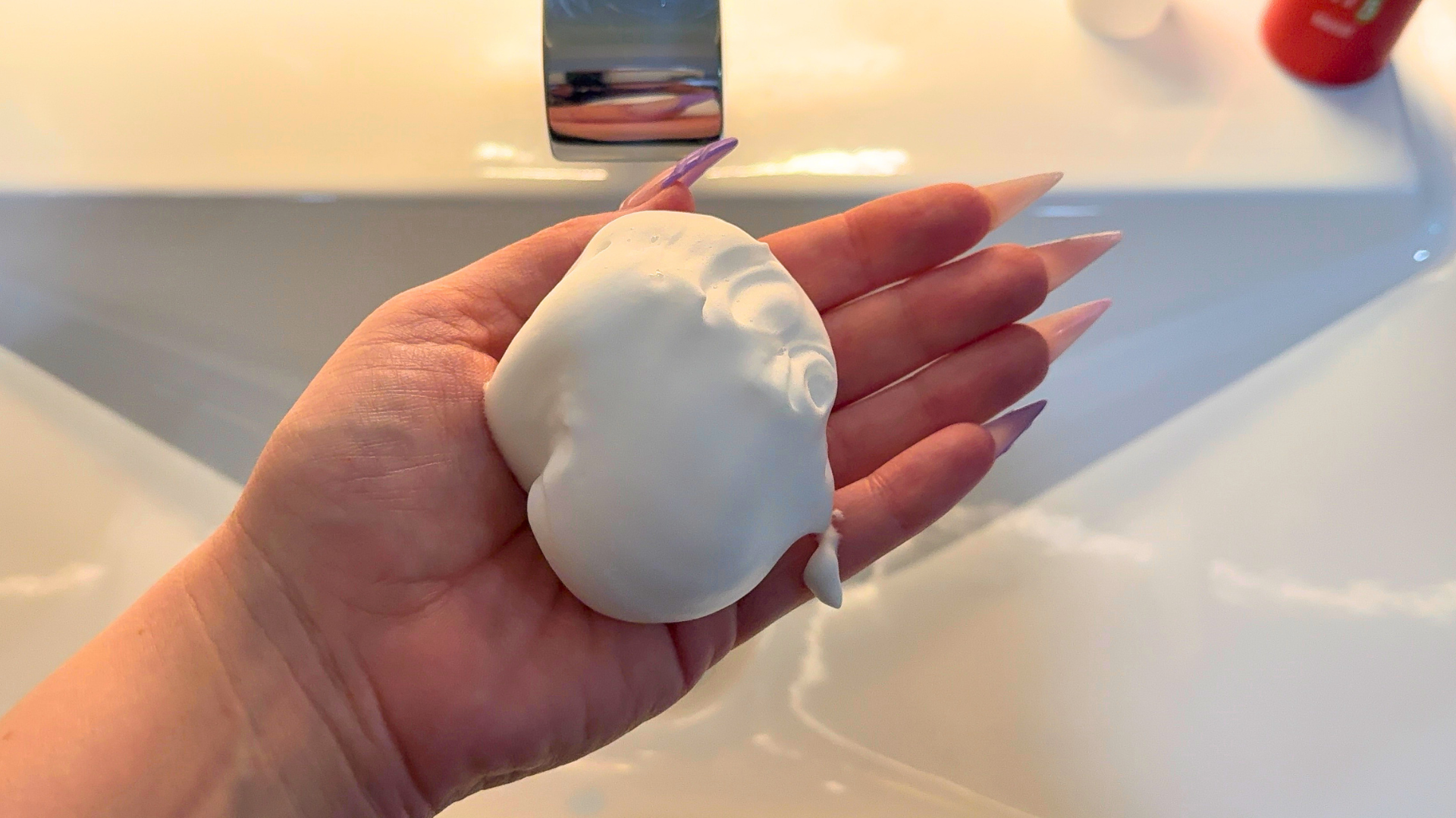 A hand holding a palm-sized amount of white foam mousse over a bathroom sink