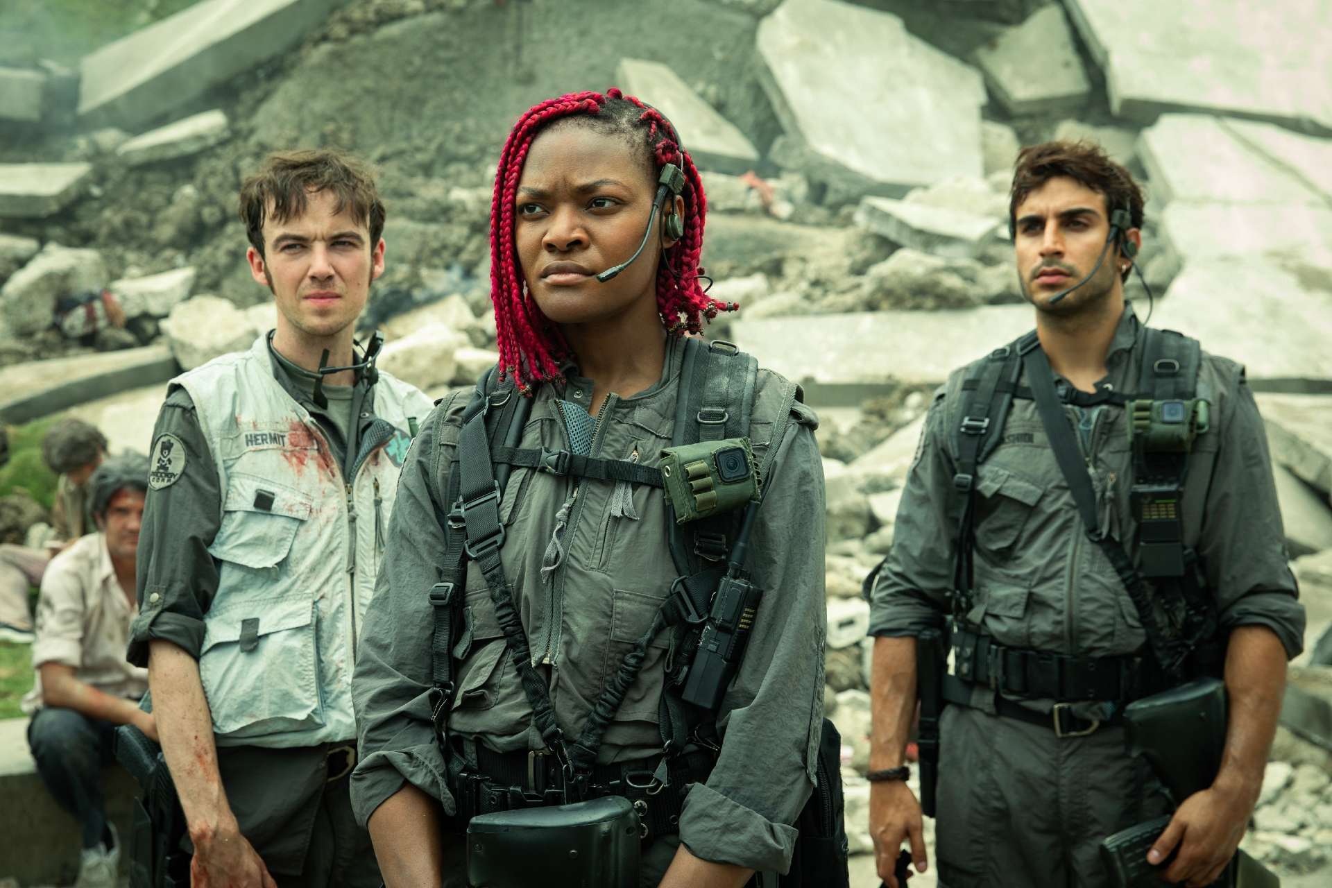  Earth. Three people are standing together in front of a large pile of rubble. They are each wearing a gray jumpsuit, utility belt, backpack, and a headset with a mic.
