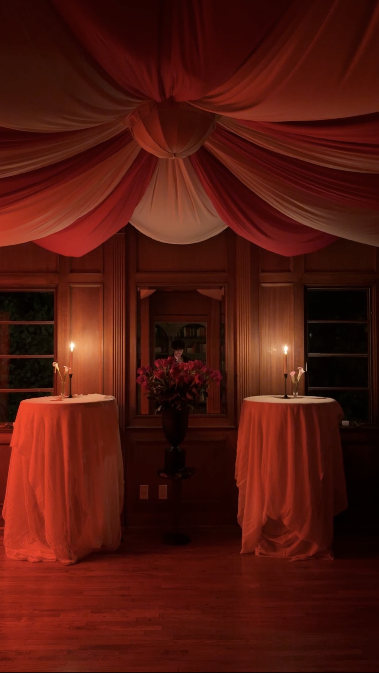 A space decorated for halloween with a circus-like tent ceiling with red and white curtain panels billowing from the ceiling, and two bar tables with red lights shining on them and candles on top