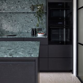Modern black kitchen with green splashback and worktop.