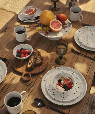 outdoor wooden dining table with speckled plates, bowls and mugs
