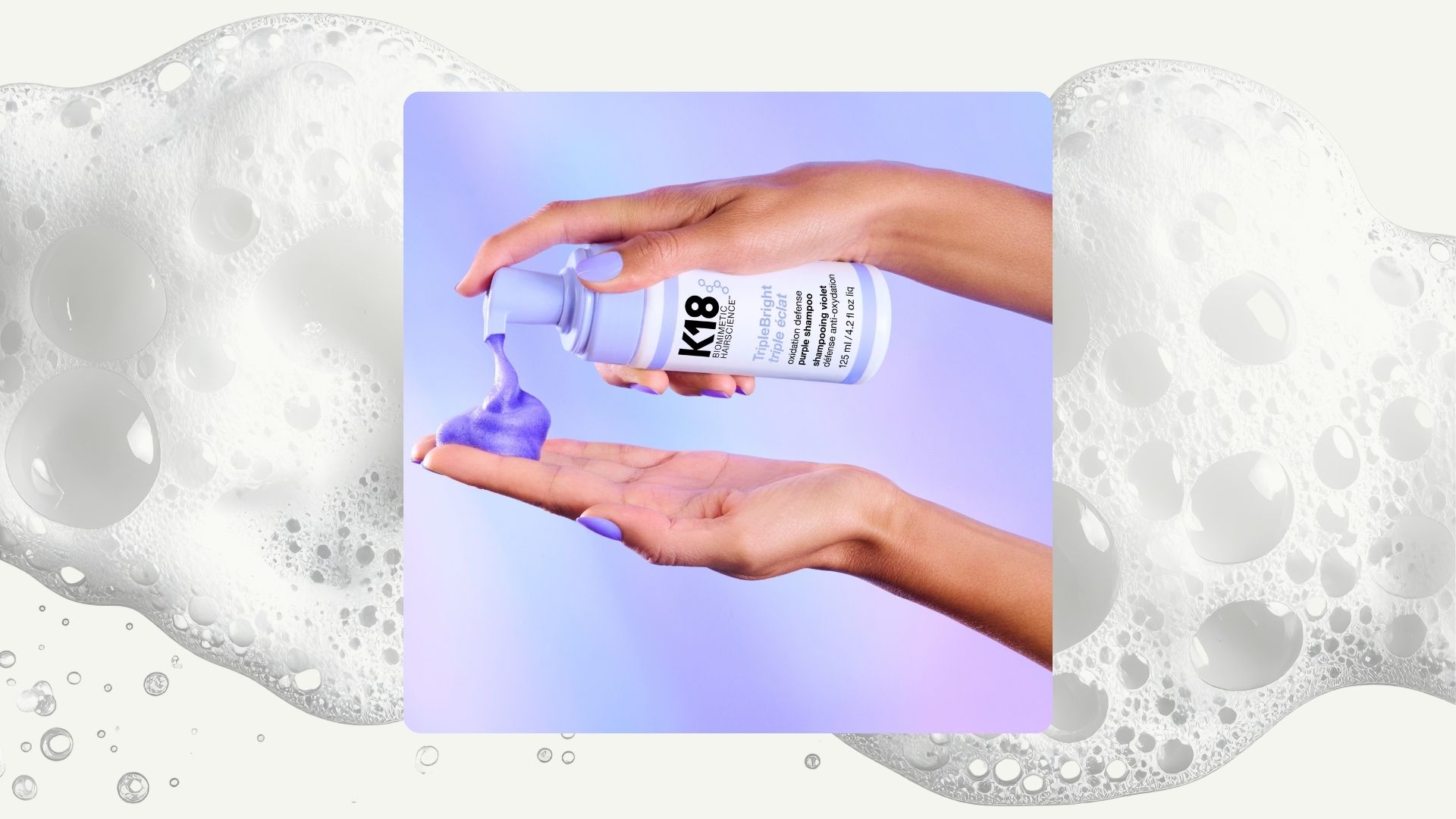 A foamy backdrop with an image of two hands holding a bottle of K18 Triplebright purple shampoo, with the foam coming out onto one hand