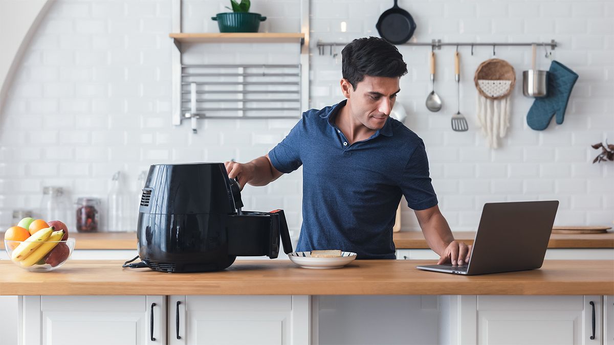 Man cooking with an air fryer while using a laptop 