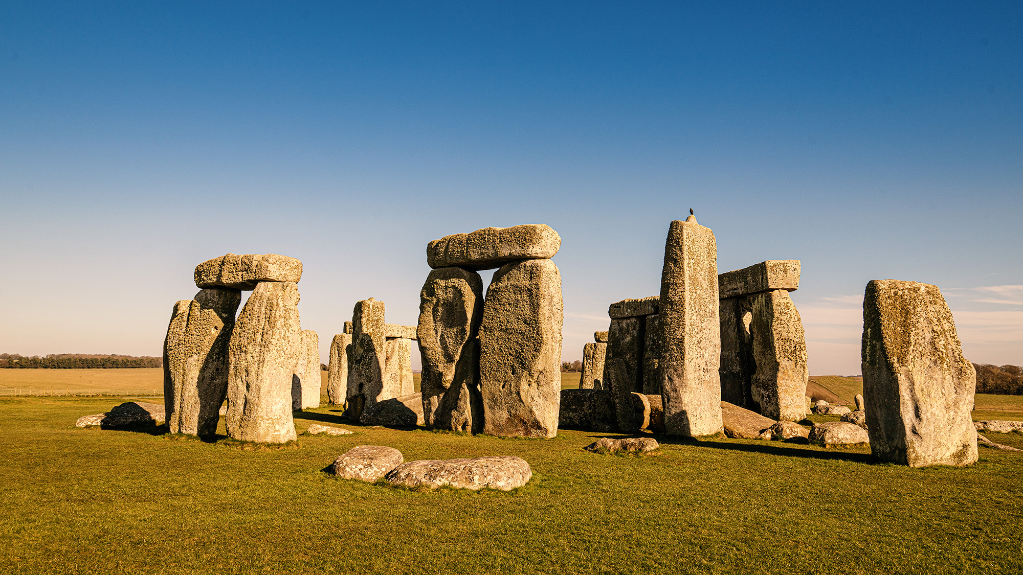 Standing stones at Stonehenge in sunlight with blue sky