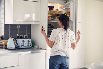 Woman looking in the fridge whilst using smartphone