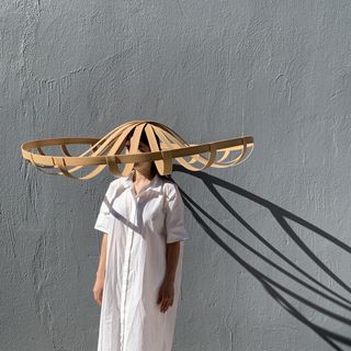 A model wearing a white dress and an oversized straw hat designed by Stephen Burks