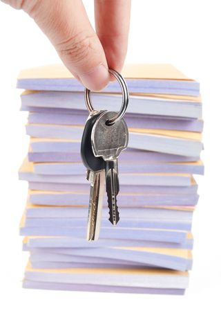 Stock photo of keys dangled in front of a stack of papers.