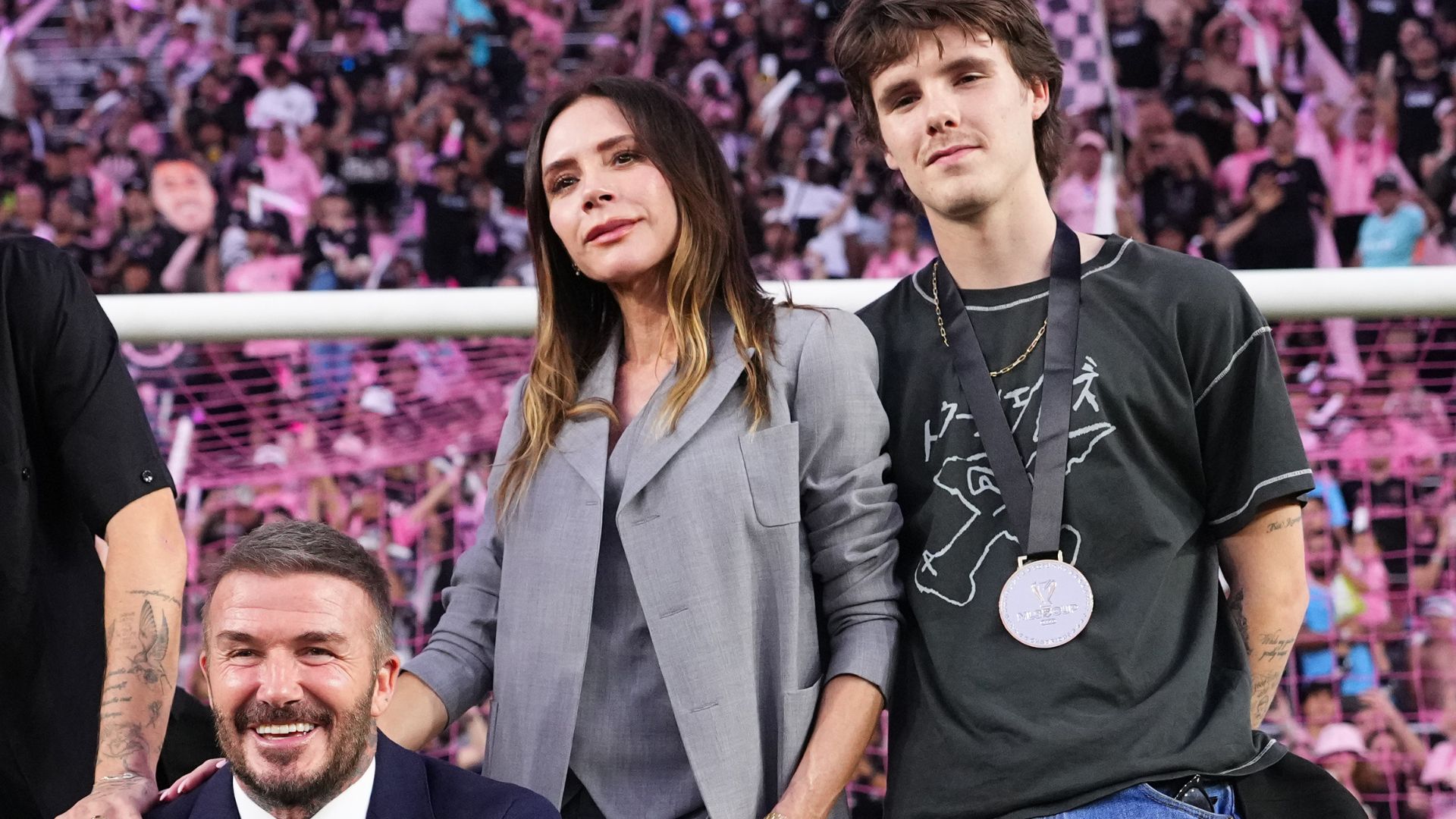 Victoria Beckham stands alongside David Beckham wearing a grey three-piece suit with skinny trousers and black peep-toe shoes.