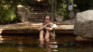 Alycia Debnam-Carey as Milla sitting in a pool holding a book and looking sad and thoughtful.