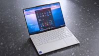 A Lenovo Yoga Slim 7i Ultra (Gen 11) Aura Edition laptop with a sleek design is open on a speckled gray surface. The screen displays a desktop with icons, set against a calming ocean background.