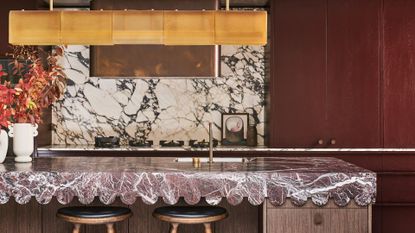 A kitchen with burgundy countertop in a wave design, and burgundy cabinets, with a gold-toned pendant above