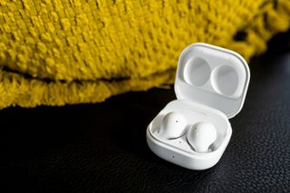 A pair of white Samsung Galaxy Buds next to a yellow jumper