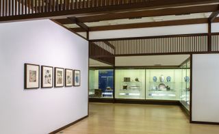 A museum with glass cases filled with Japanese crockery and painting on the walls..