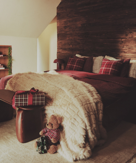 Cozy mountain cabin bedroom featuring plaid bedding, a faux fur throw blanket, and a charming stuffed teddy bear toy.