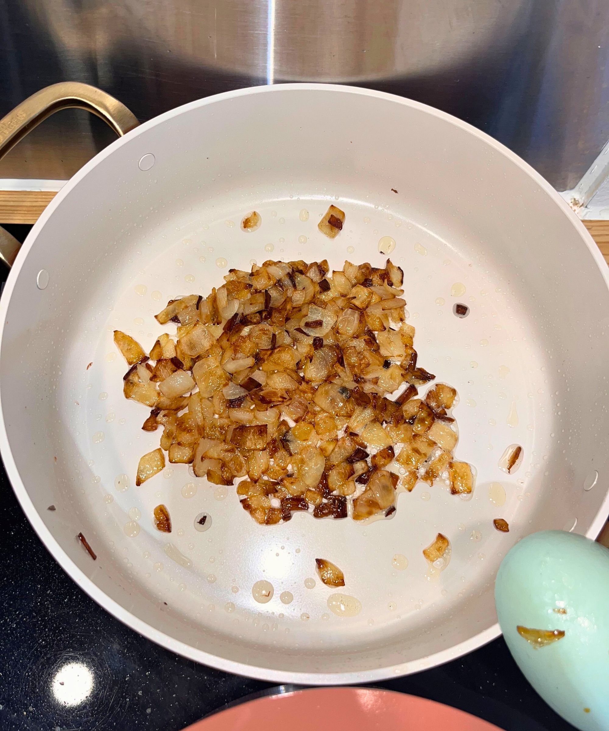 Frying onions in the Our Place frying plan from the Essentials 11-Piece Set. Most are golden-caramel color, and some are darker