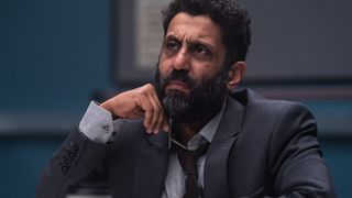 Actor Adeel Akhtar sitting in a darkened police interview room, wearing a worn grey suit and tie, in new TV drama Showtrial season 2 