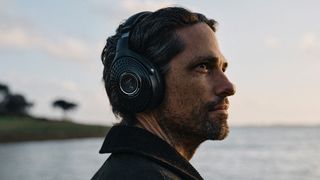 A man near the sea, wearing headphones, looks out into the distance. 