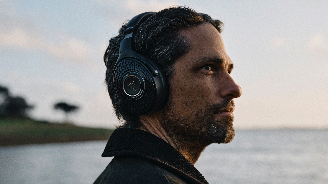 A man near the sea, wearing headphones, looks out into the distance.
