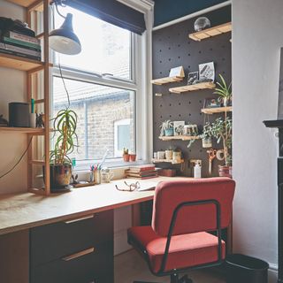 A home office with the built-in desk featuring plenty of storage facing the window and a pegboard to the side