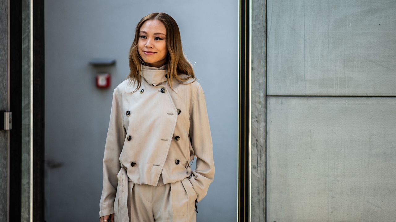 an attendee at milan fall winter 2025 fashion week wearing a short trench coat and trousers