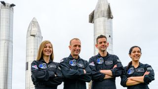 four people in black flight suits with arms crossed. behind are three silver starship spacecraft